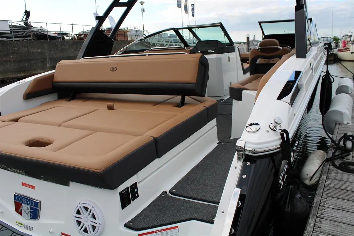 Interior of a Cobalt R6 boat featuring beige cushioned seating, gray deck, and marine controls on the side.